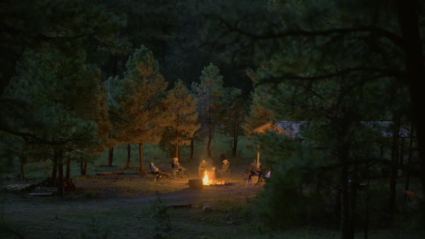 Group of men sitting around a campfire in a clearing on the forest at night