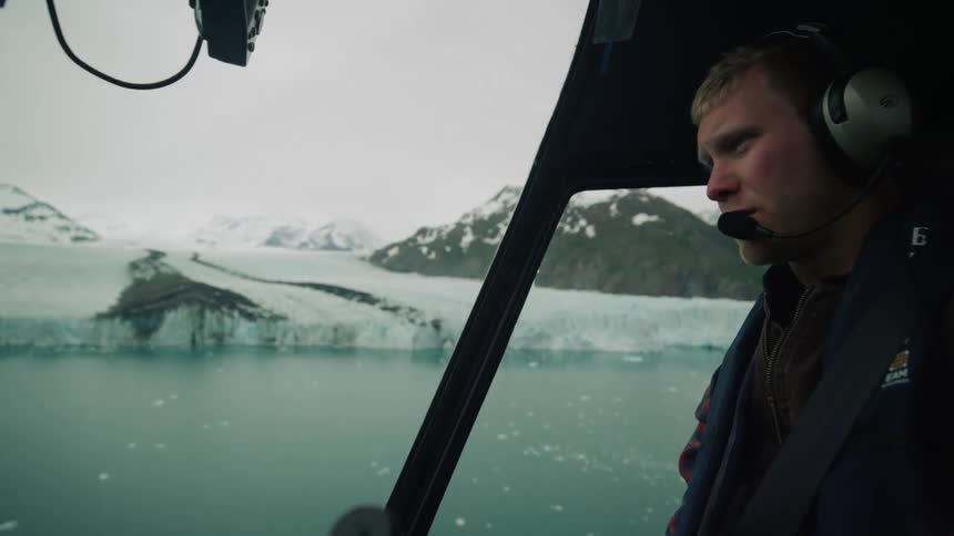 Man steers vehicle over water near glacier as rotor flickers against sky overhead