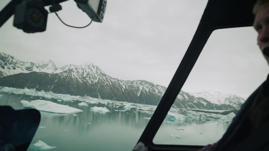 Male pilot operates helicopter over sea with glaciers
