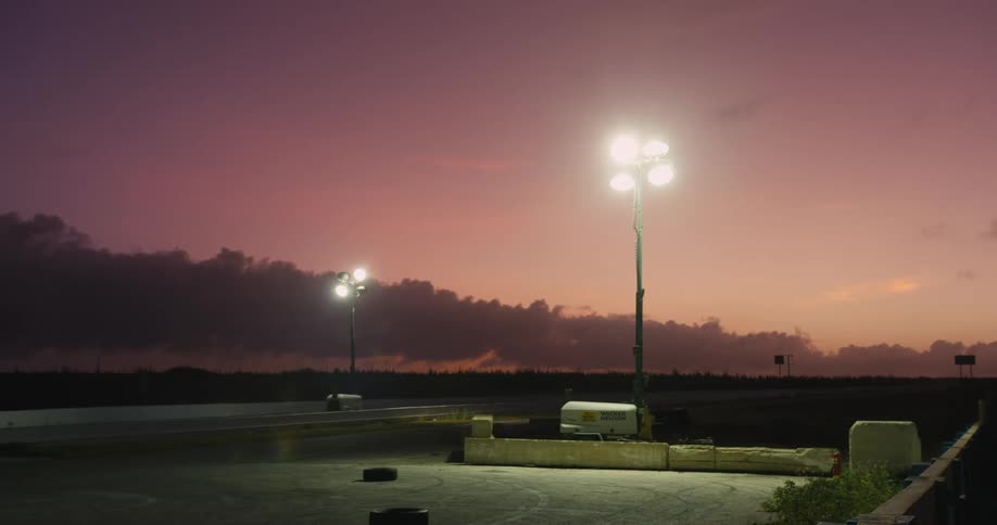 Bright lights on posts glow at an empty track at sunset