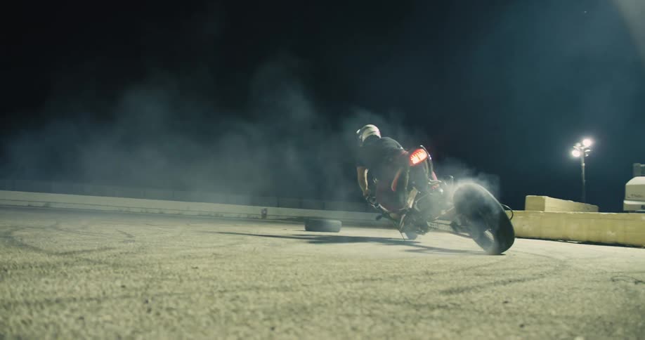 Man burning the rubber on the tires of a motorcycle on a track at night