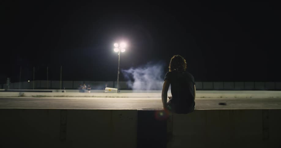 Spectators watch motorcycle race along track at night under spotlights