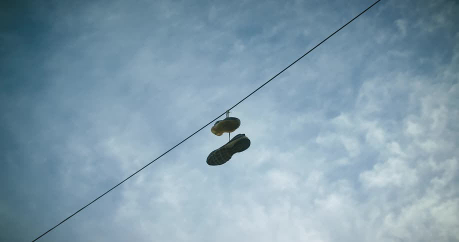 A pair of shoes is hanging from a wire high in a cloudy sky