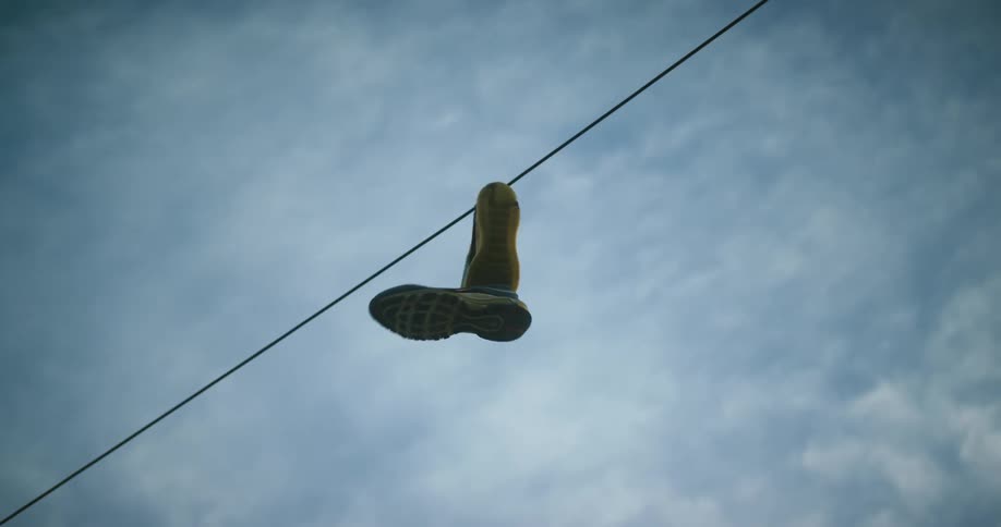 A pair of shoes with their shoestrings tied together hang from a power line