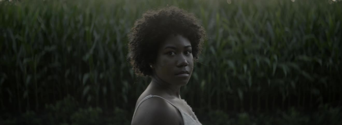 Woman standing by a corn field turns her head and stares