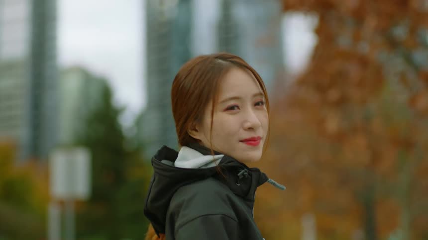 Young woman looks at the camera smiling in front of buildings in the city at fall