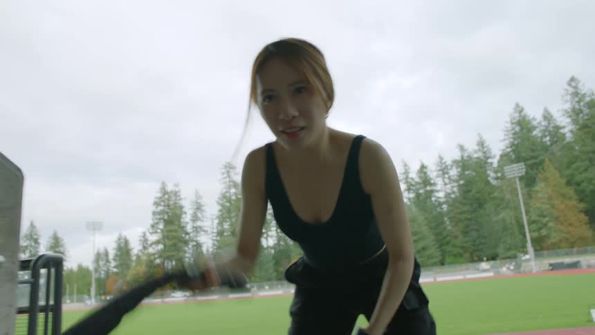A woman exercises with battle ropes in the corridor of the stands of an athletics field on a cloudy day