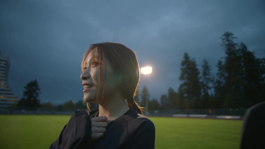 Two teenage girls are standing in a field talking and a bright light is shining in the distance