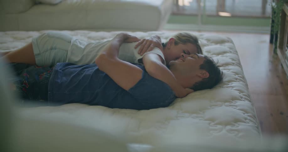 A man and woman smile at one another while embracing as they lie together on a bed