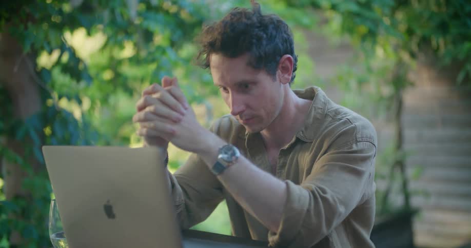 Man sits outdoors thinking and typing on laptop