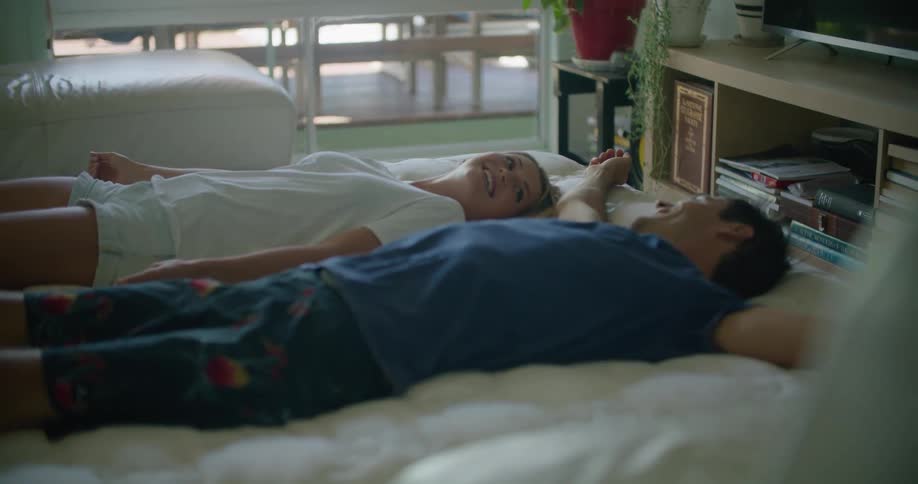 Couple lies down on bed in room near television