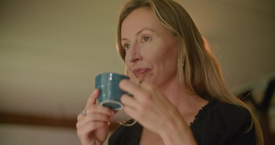A woman smiles after taking a sip from her coffee cup