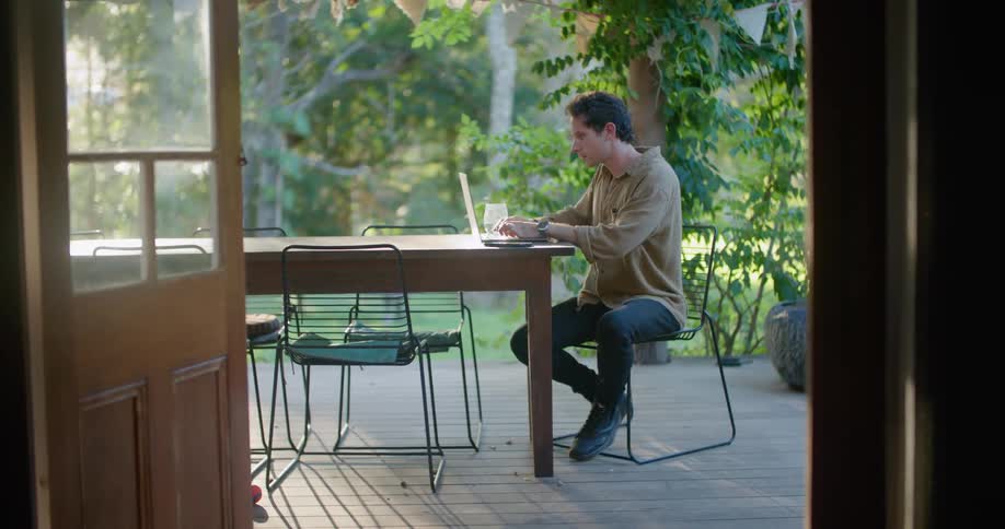 A man is sitting at a table outside typing on a laptop computer