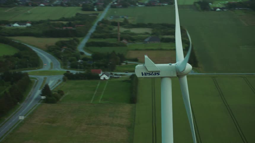 Aerial view of a wind turbine spinning next to farms and agricultural lands
