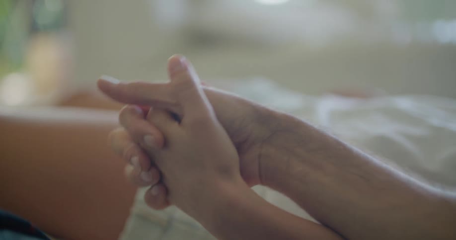 Couple holding hands while resting in bed at home