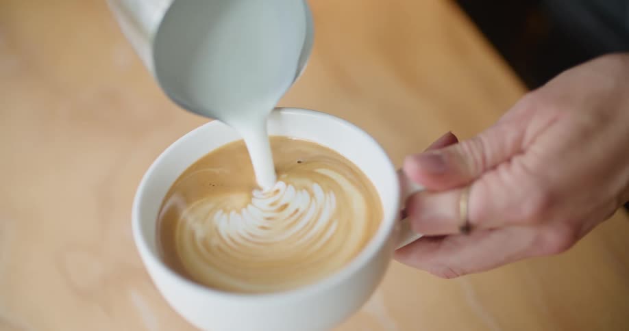 A person is pouring cream in their coffee and makes a design