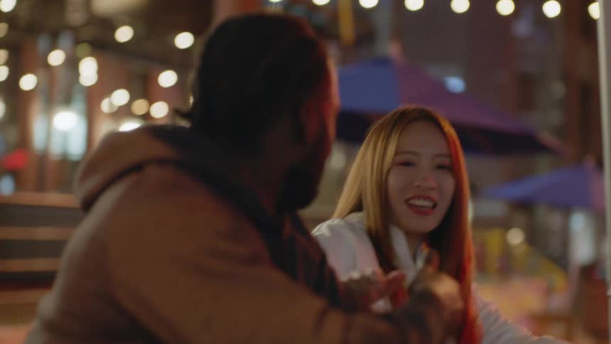 Friends meeting at a table of an outdoors restaurant on the city at night
