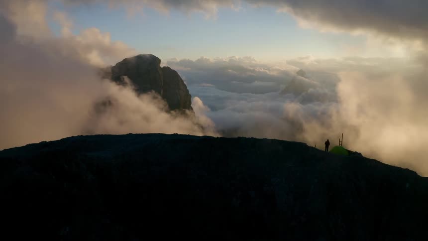 Sunlight shines on clouds as they move over mountains high in the sky
