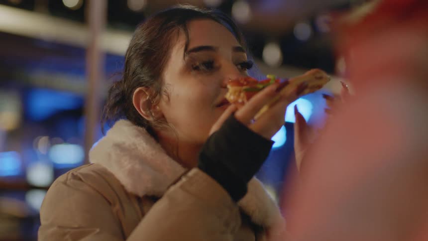 Young woman eating pizza with friends on an outdoors restaurant in the city at night