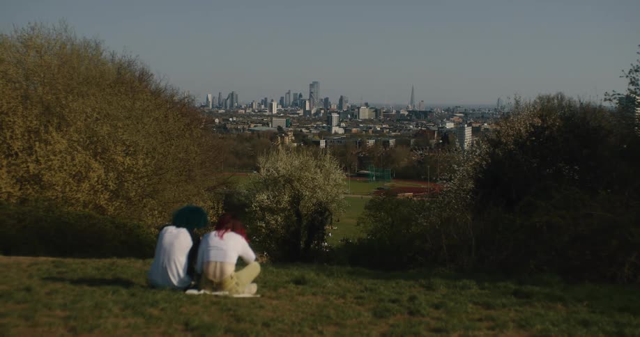 Couple sit on ground in park with city in background