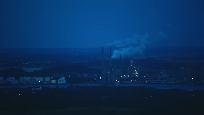 Smoke rises from smokestacks on factory sitting on river on misty day
