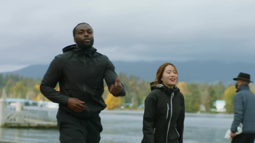 Young friends jogging next to a lake in a park at fall