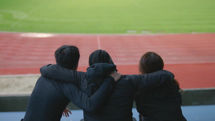 Three people sit together in the bleachers of the race track