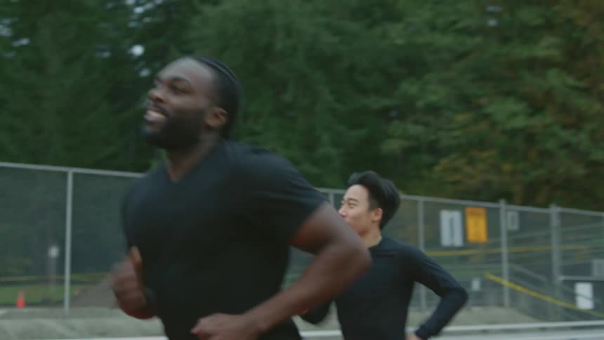 A man runs along an athletics track to reach the side of a man jogging ahead of him