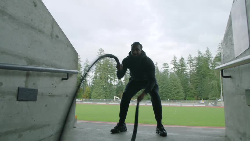 A man is exercising by pulling rope up and down near the field