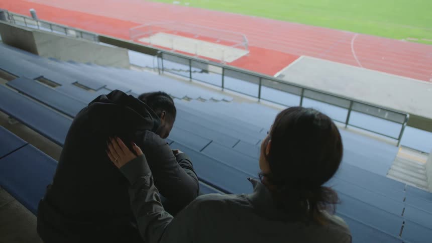 Man and woman have a conversation in the stands next to a track