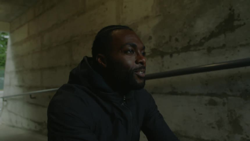 A man squatting down in a tunnel encourages a woman working out with heavy ropes