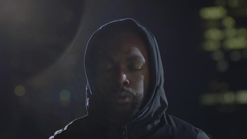 A man standing outside at night pulls his hood off and takes a couple of deep breaths