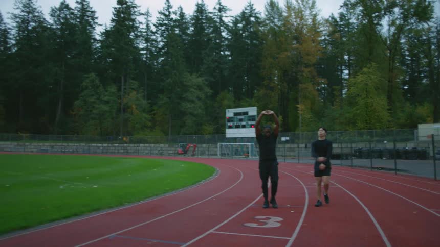 Two men stretch and warm up while walking on the track