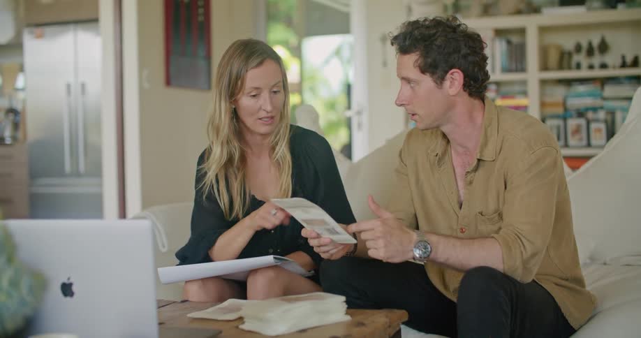 A man and woman sit on a couch in a home and talk as they look at pamphlets