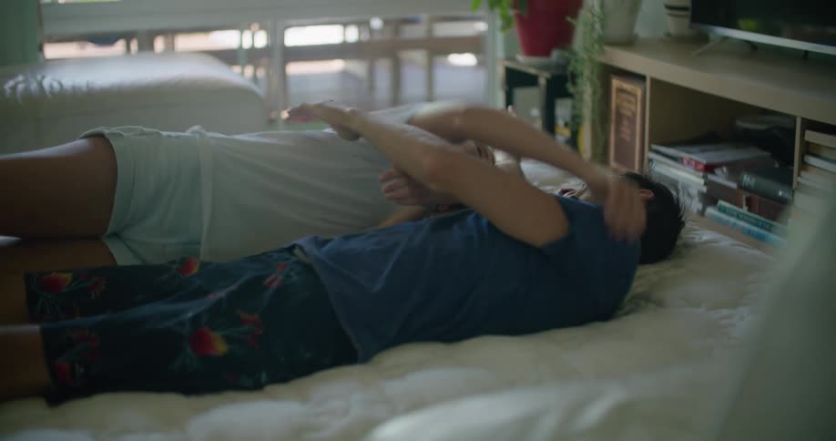 A laughing woman and man embrace while lying together on a bed
