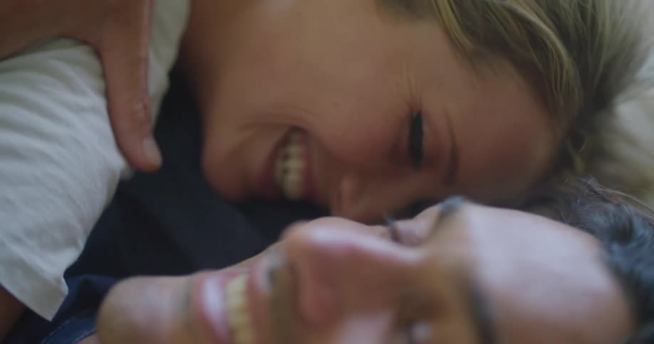 A man with his arm around his wife as they lie in bed smiling and laughing