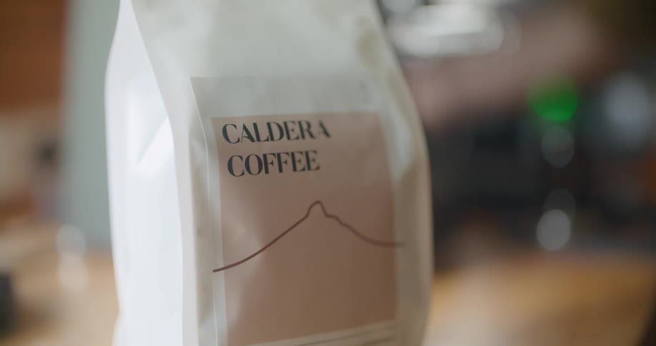 A bag labeled caldera coffee sitting on a table is picked up by someone
