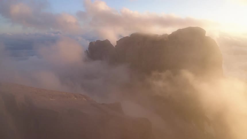 The sun is shining on a mountain ridge high in the sky among the clouds