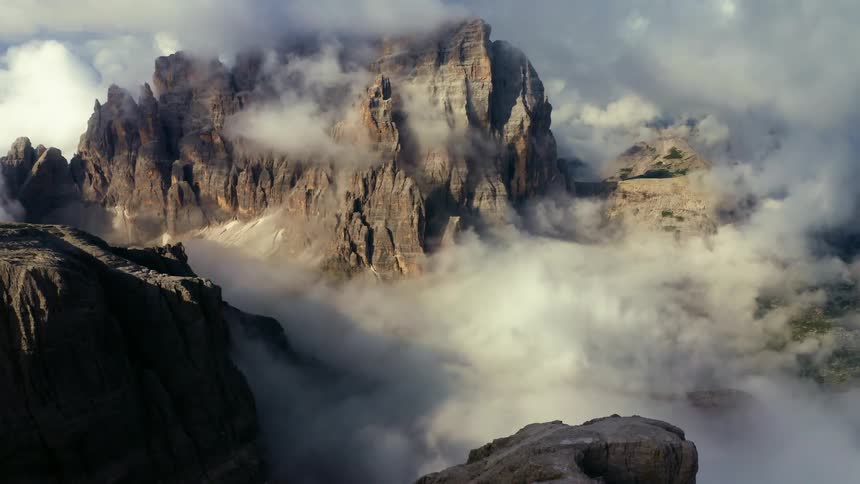 An aerial view of rocky mountains with low clouds and fog during the daytime