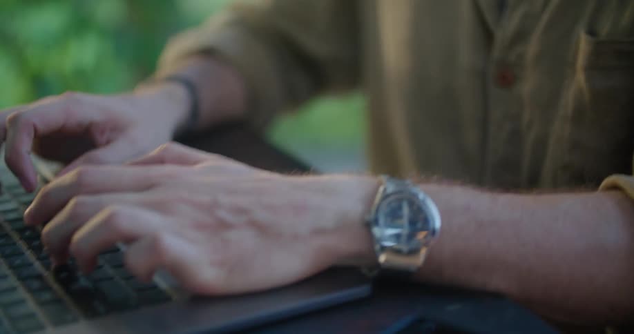 Man sitting at a table outdoors in the morning typing on a laptop