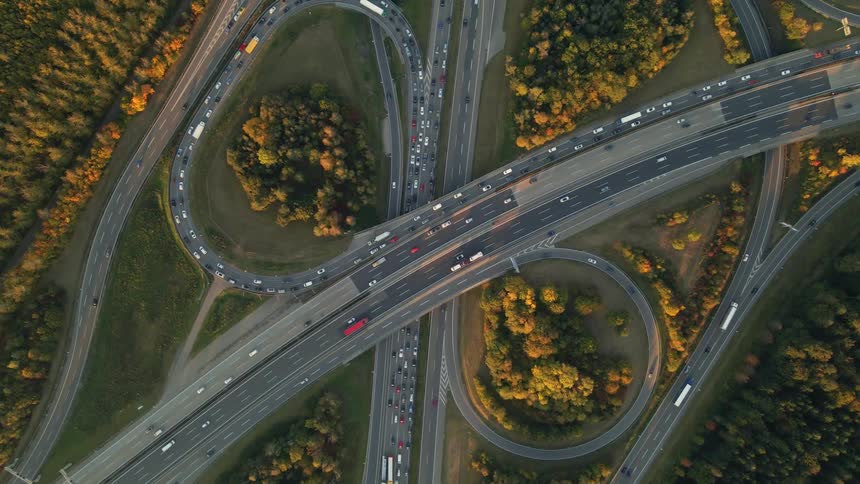 Vehicles flow along overpass and highways and sit in traffic jam surrounded by forest