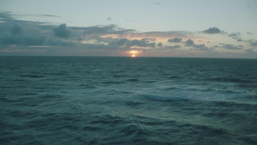 The sun is on the horizon shining through the clouds over the ocean