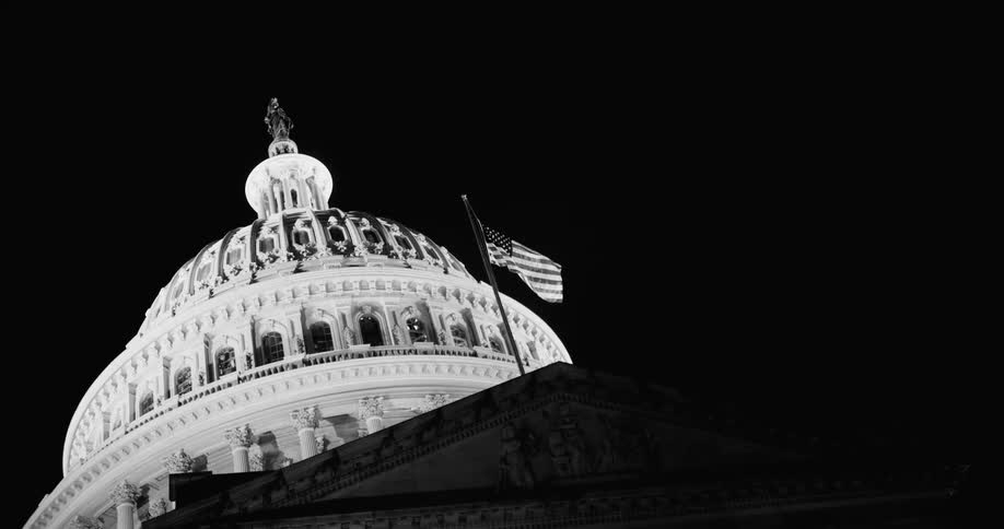 American flag flying near the dome of the capitol building at night