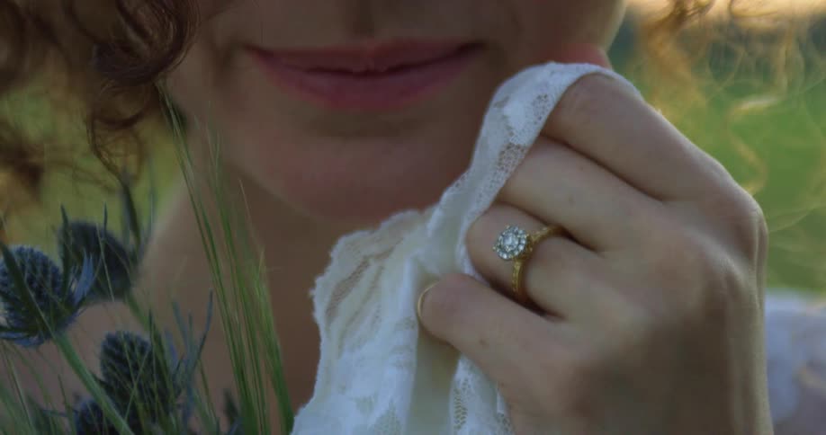 Close portrait of a young bride in a wedding gown while holding wildflowers outdoors in the early evening