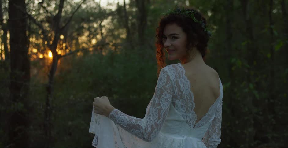 Bride wearing a white wedding dress standing in front of the sunset in the forest