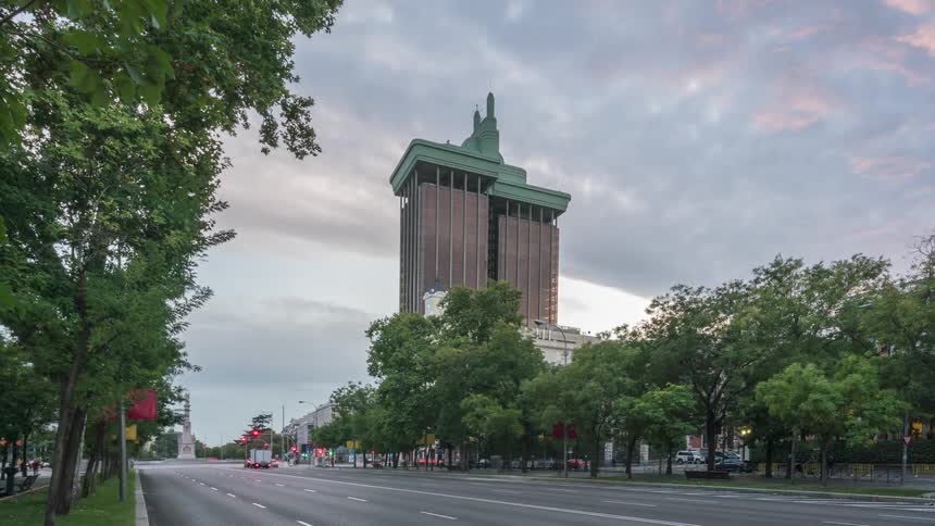 Traffic flows along city street through intersection under cloudy sky