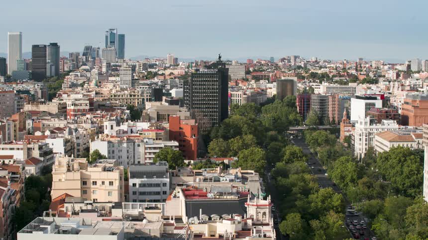 Traffic moves on city streets and overpasses with skyscrapers and hills behind