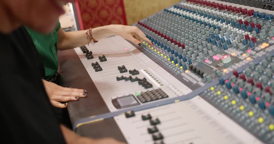 Two people are using a soundboard in a studio