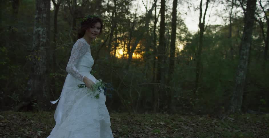 A bride is walking next to a woodland area while wearing her wedding gown at dusk