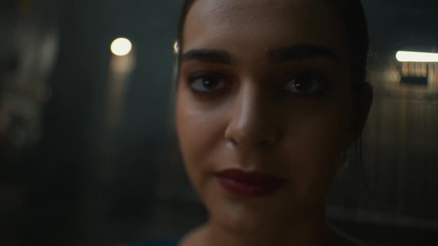 Young elegant woman standing on a dimly lit room looking at the camera